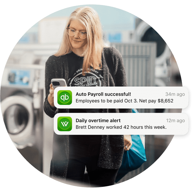 An owner of a laundromat looking at two notifications on her mobile device: Auto payroll notification and daily overtime alert notification.